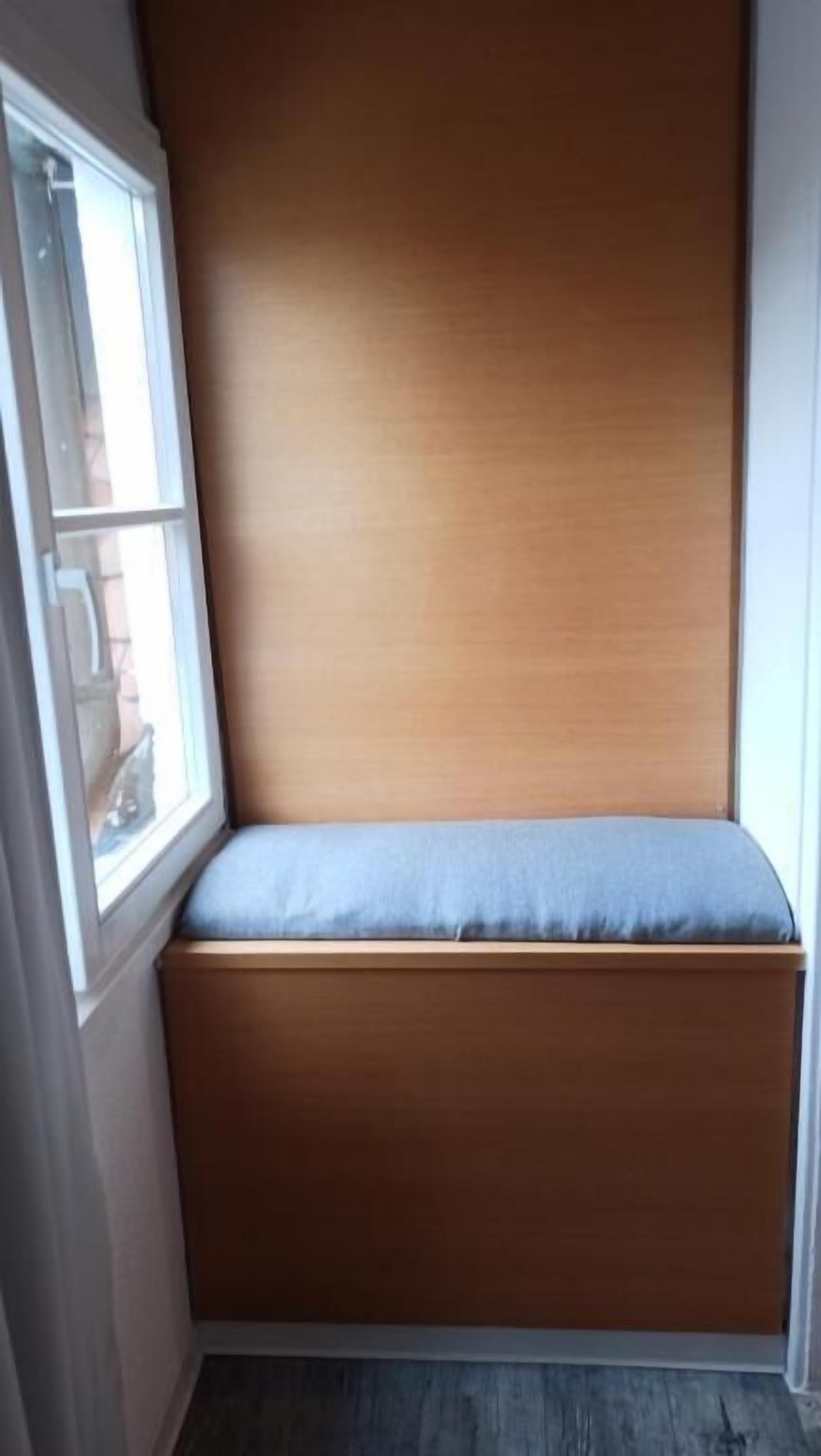 Ein Eckzimmer mit einer fest eingebauten Bank an der Wand, einem Fenster und einer Tür.