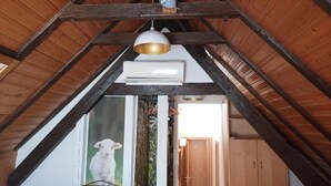A room with a sloped ceiling, wooden beams, a white air conditioning unit, and a hanging pendant light. - Gasthof Hirsch (Gengenbach)
