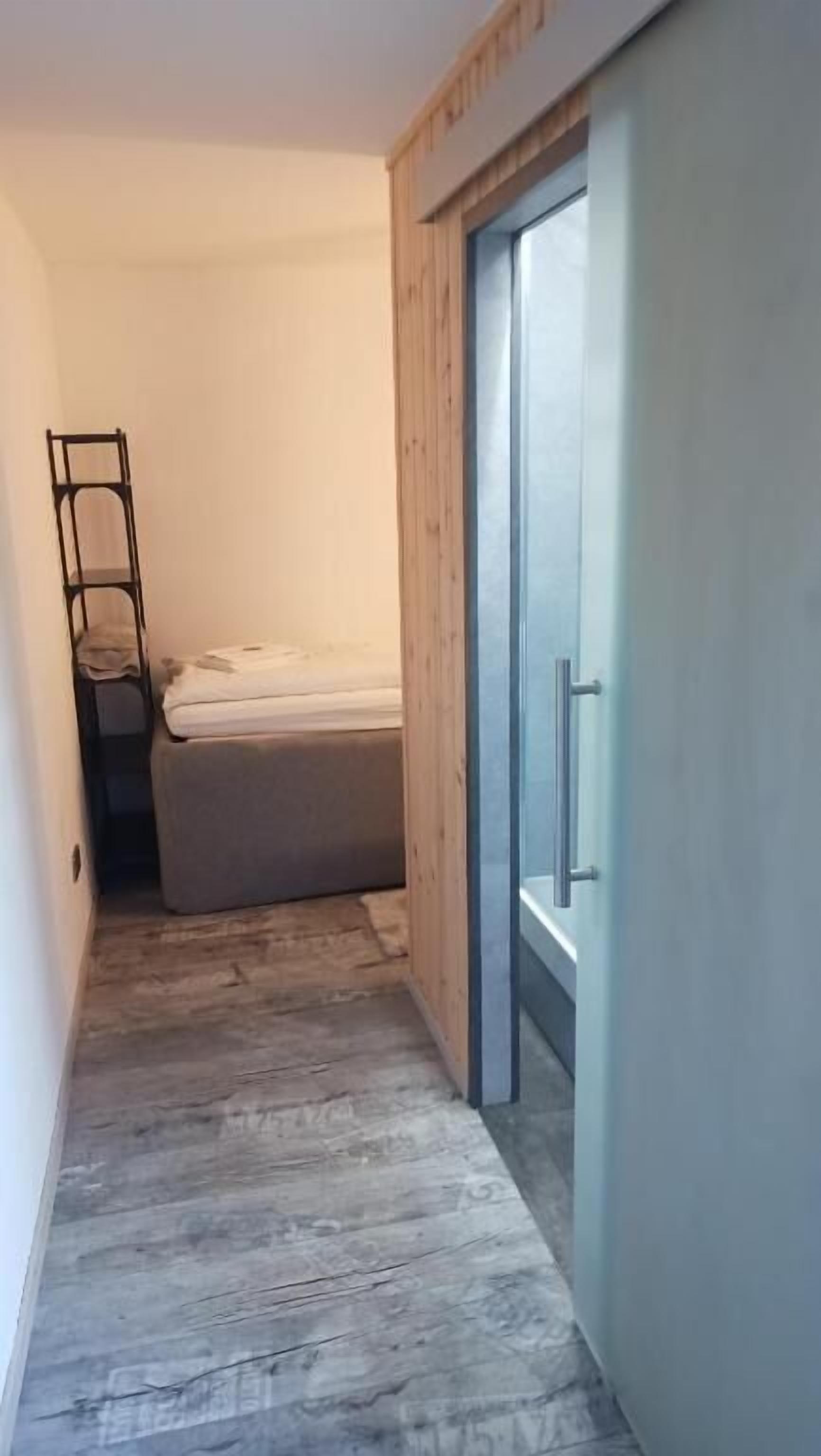 A narrow hallway with a bed, a wardrobe, and a ladder against the wall.