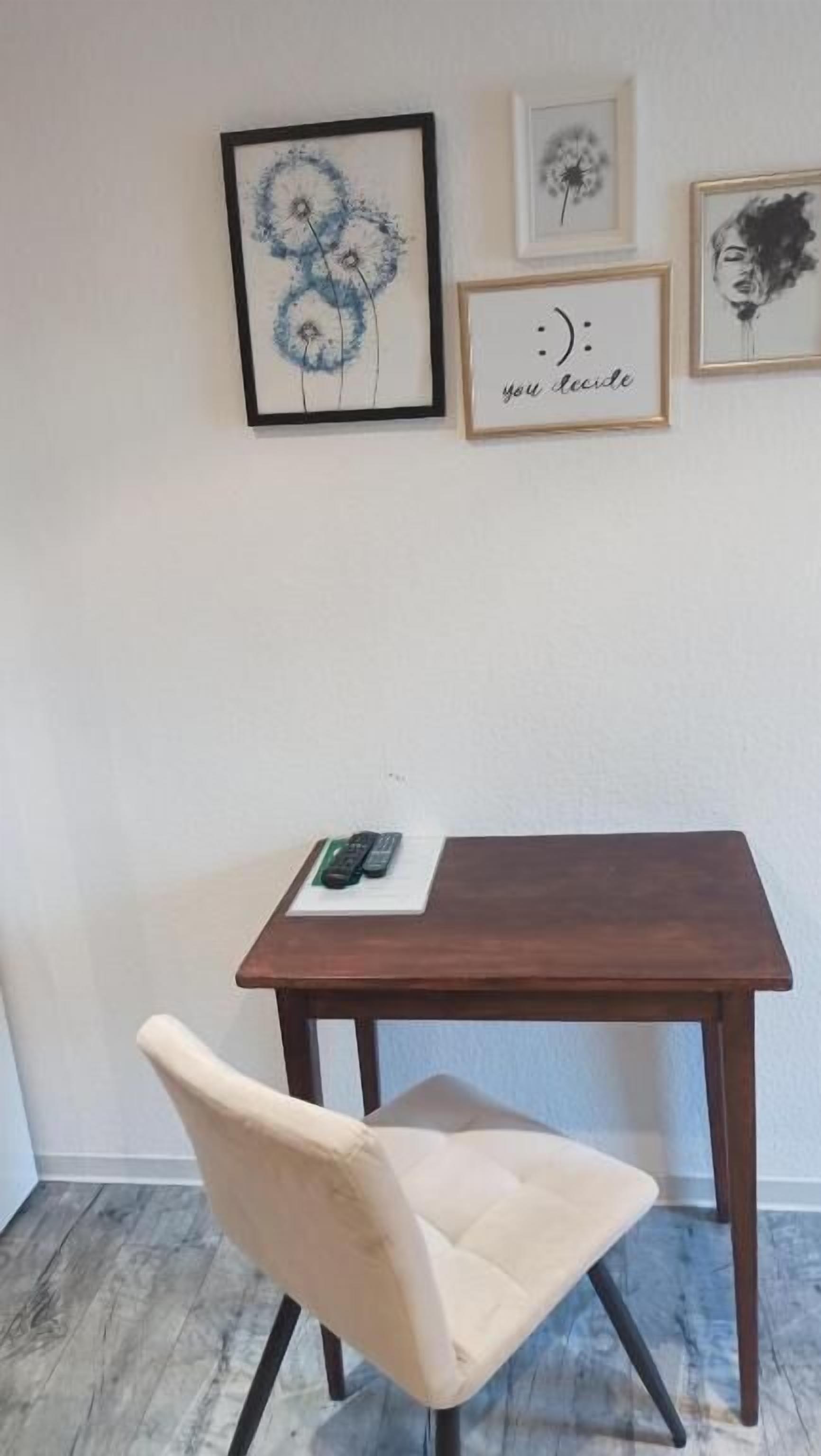 A small room with a wooden table, a single chair, and three framed artworks on the wall.