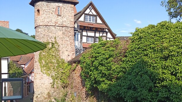 A historic stone tower and a traditional half-timbered building with a cobblestone pathway and greenery. - Gasthof Hirsch (Gengenbach)