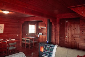 A cabin interior with a dining area, a sofa, a fireplace, and a kitchen.