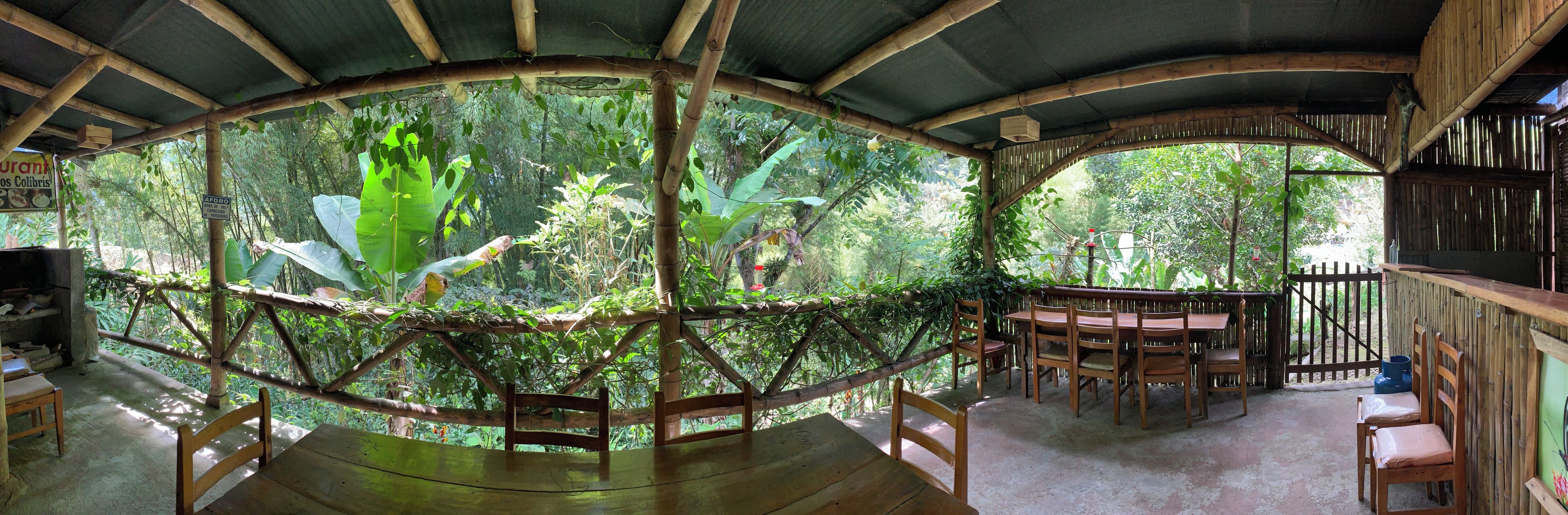 An outdoor dining area with bamboo structures, wooden furniture, and lush greenery.