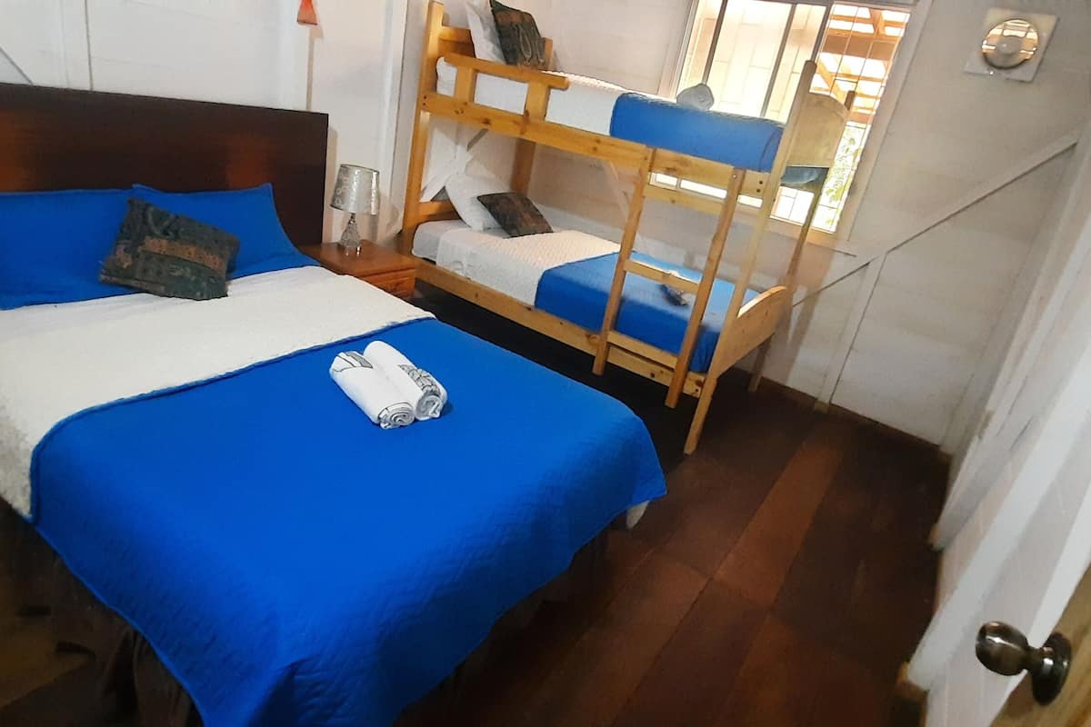 Een kamer met een bed, een stapelbed, een houten nachtkastje en een deur.