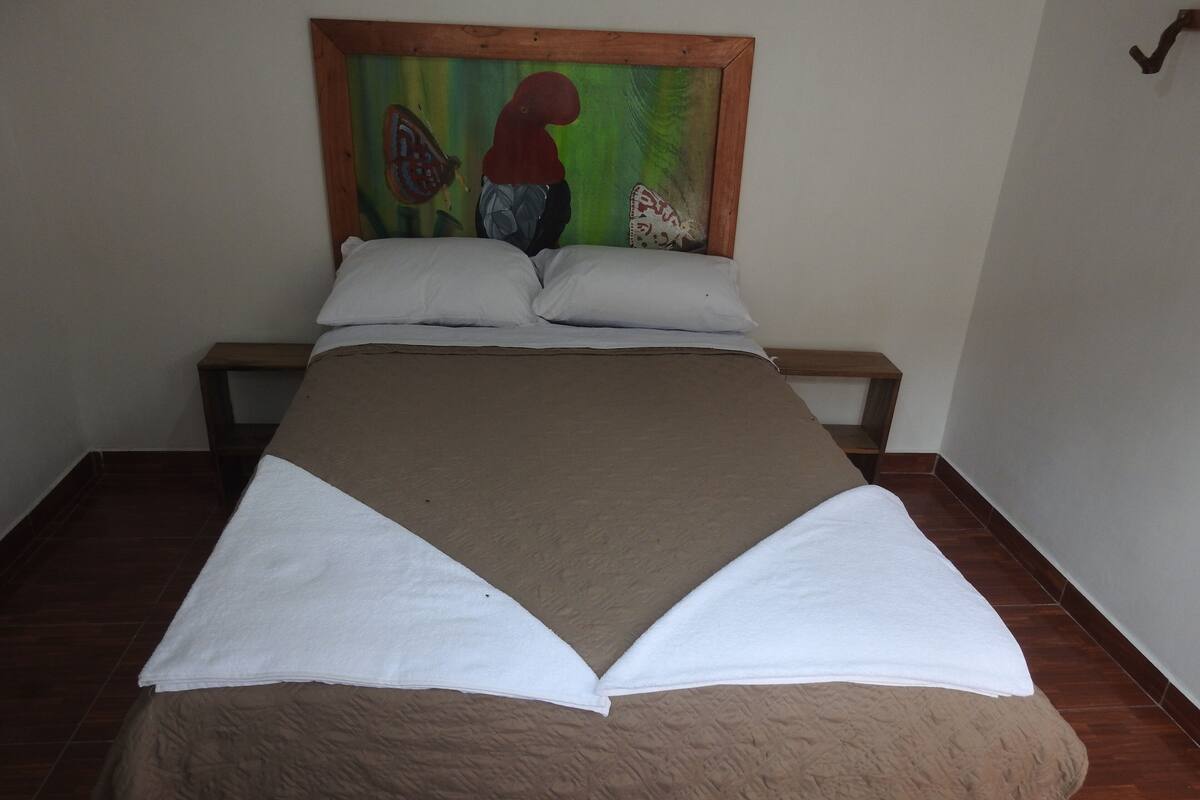 Een bed met een bruin-witte dekbedovertrek, een houten hoofdbord en een schilderij erboven.