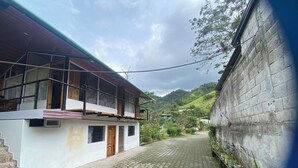 A two-story building with a balcony, a paved courtyard, and a hillside in the background. - Butterfly and Bird Julio Tours-Ecolodge (Nanegal)