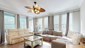 Un salón amplio con un sofá color beige, una mesa de centro de vidrio y un ventilador de techo.