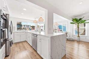 A modern kitchen with white cabinetry, a marble island, and pendant lighting. - Magical BayFRONT Home with Epic Dock and Hot Tub (Newport Beach)