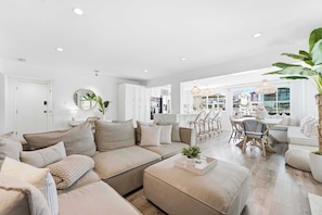 Un salon moderne avec un canapé, un pouf et un coin repas comprenant des chaises.