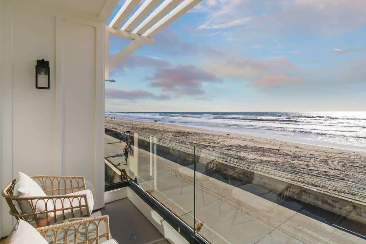 A balcony with wicker furniture, a glass railing, and a view of the beach.