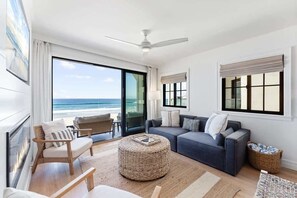 A modern living room with a large window overlooking the ocean, a ceiling fan, and a cozy seating area. - Entire Upper Oceanfront Masterpiece with Rooftop, Hot Tub + Sauna (San Diego)