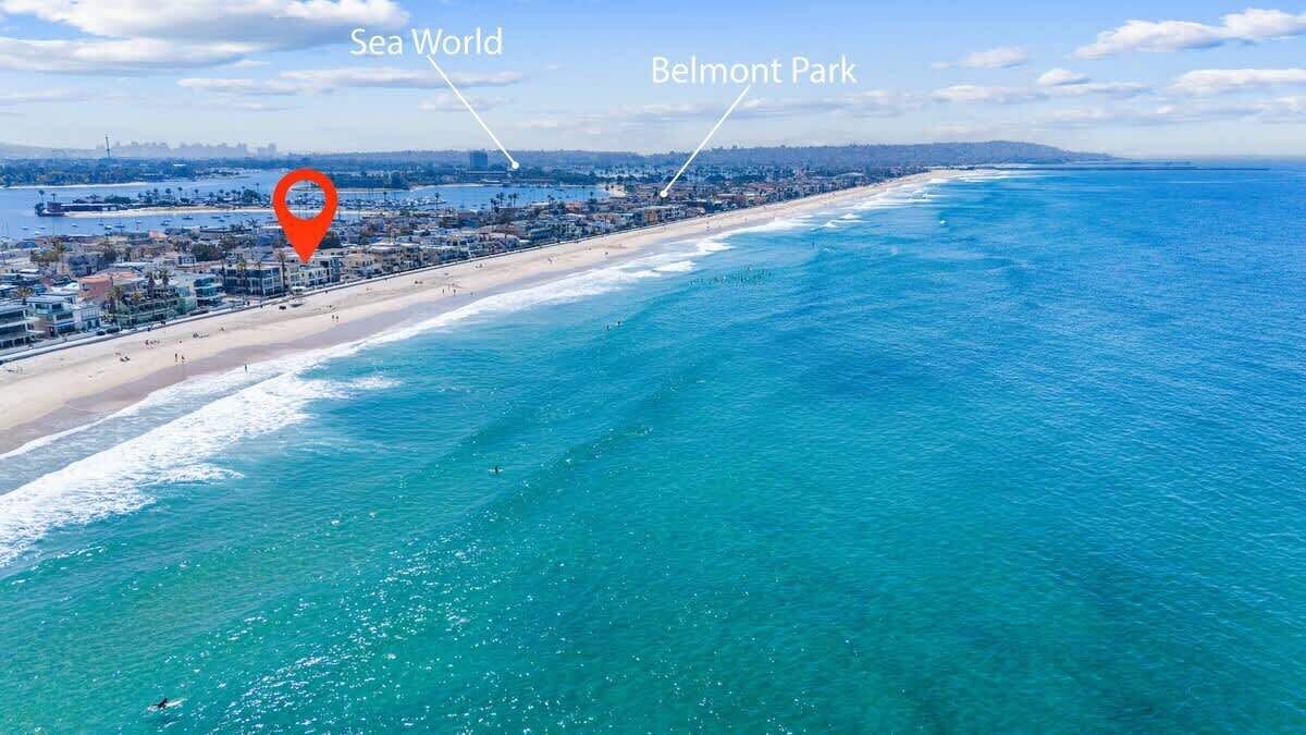 Une vue urbaine côtière avec une plage, un marqueur de localisation rouge et des panneaux indiquant « Sea World » et « Belmont Park ».