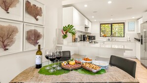 A modern kitchen with white cabinets, a dining table set with wine glasses, a bottle of wine, and a fruit platter. - Topical ocean front 2-bedroom condo with AC in charming Koloa (Koloa)