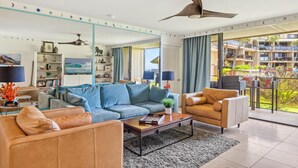 A modern living room with a sofa, armchairs, a coffee table, and a ceiling fan. - Topical ocean front 2-bedroom condo with AC in charming Koloa (Koloa)