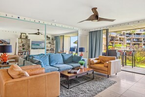 Ein modernes Wohnzimmer mit einer Couch, Sesseln, einem Couchtisch und einem Deckenventilator.