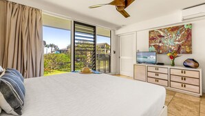 A bedroom with a bed, a television, a ceiling fan, a sliding glass door, and a painting. - Topical ocean front 2-bedroom condo with AC in charming Koloa (Koloa)