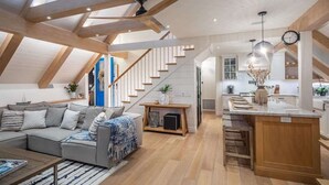 A modern loft with a high ceiling, exposed beams, a living area with a sofa and coffee table, a kitchen with a central island, and a staircase. - Neptune Ocean View Masterpiece (Encinitas)