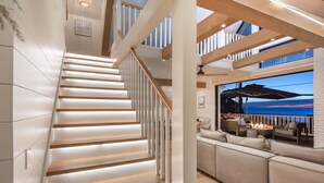 A staircase with wooden steps and white railings, leading to a living area with a sofa and a view of the ocean. - Neptune Ocean View Masterpiece (Encinitas)