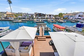 A marina with boats docked, a wooden deck with seating, and buildings in the background. - Stunning Bayfront Home with Epic Dock on Peninsula! (Newport Beach)