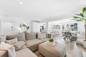 A modern living room with a sofa, ottoman, and dining area with chairs. - Stunning Bayfront Home with Epic Dock on Peninsula! (Newport Beach)