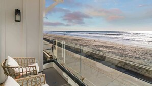 A balcony with wicker furniture, a glass railing, and a view of the beach. - Luxury S Oceanfront Unit with Rooftop & Hot Tub + Sauna (San Diego)