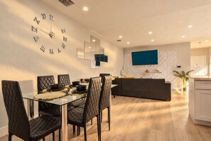 A modern dining area with a glass table, black cushioned chairs, and a wall clock. - Game Backyard + Soaking Pool - 10 Min to Brickell (Miami)