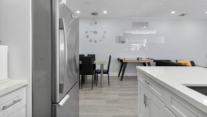 Une cuisine moderne avec un réfrigérateur en acier inoxydable, une table à manger avec des chaises et une horloge au mur.