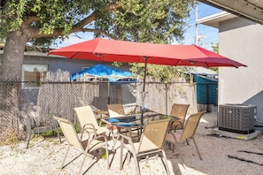 Eine Terrasse im Freien mit Tisch und Stühlen, einem roten Sonnenschirm und einer Klimaanlage.
