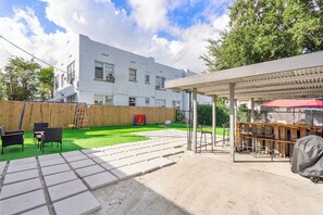 Patio trasero con mobiliario exterior, cerca de madera y edificio blanco al fondo.