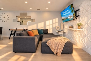 Ein modernes Wohnzimmer mit einer Eckcouch, einem Flachbildfernseher und einer Wanddekoration.