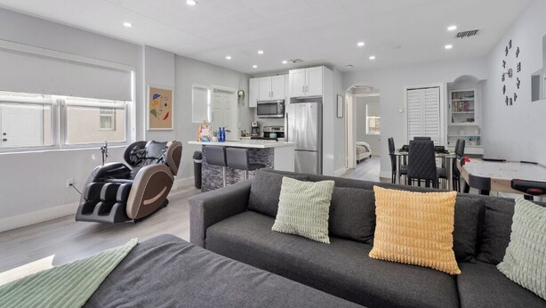 Un salon moderne avec un canapé gris, un fauteuil massant et un coin repas comprenant une table et des chaises blanches.