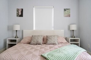 Un dormitorio con cama, dos mesitas de noche, dos lámparas y dos cuadros colgados en la pared.