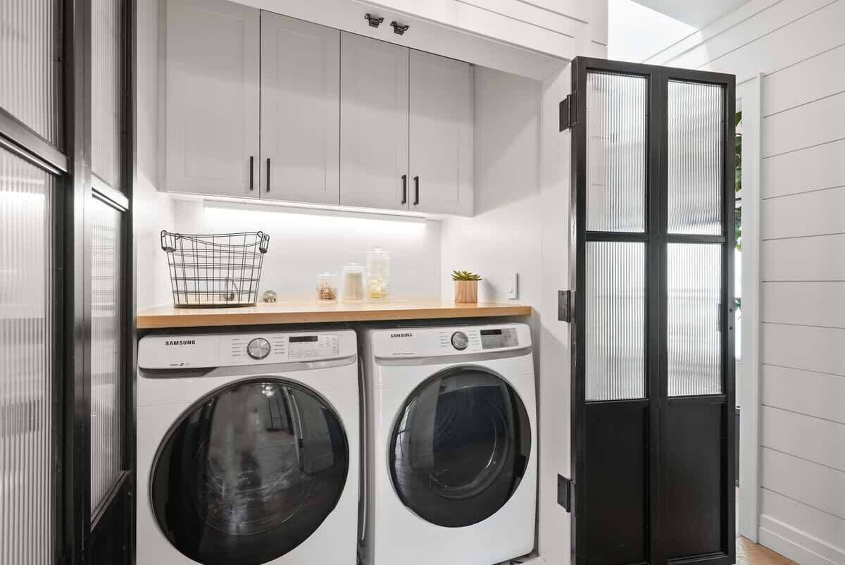A laundry room with two Samsung washing machines, a wooden countertop, and a black door with glass panels.