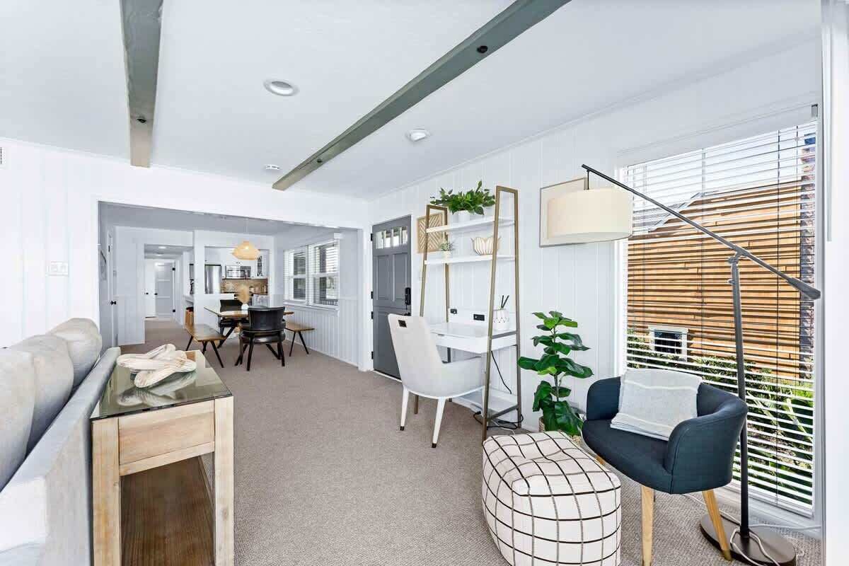 Un salon moderne comprenant un canapé, une table basse, un coin repas avec une table et des chaises blanches, et une grande fenêtre avec des stores.