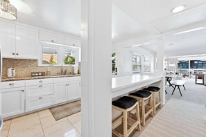 A modern kitchen with white cabinets, a granite countertop, and a bar area with stools. - Stunning BayVIEW Home with Epic Waterfront Views! (Newport Beach)