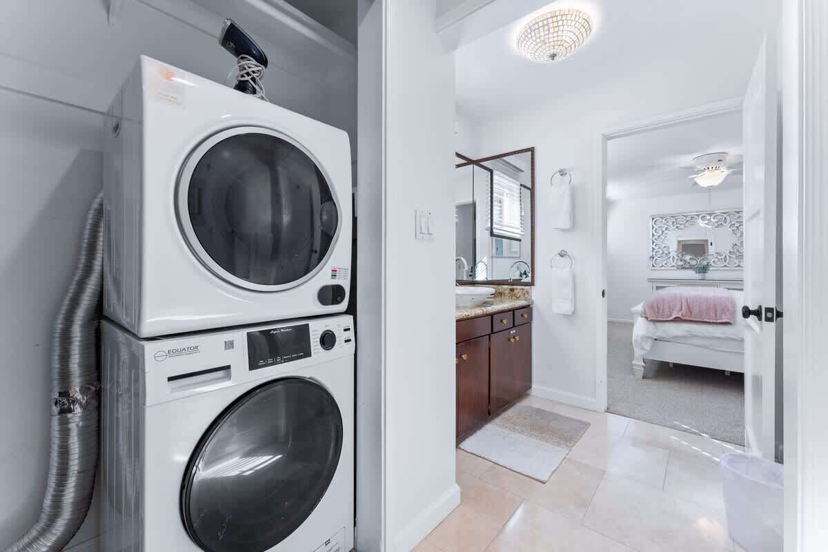 A laundry room with stacked washing machines and dryers, a kitchen with a countertop and cabinets, and a bedroom with a bed and a nightstand.