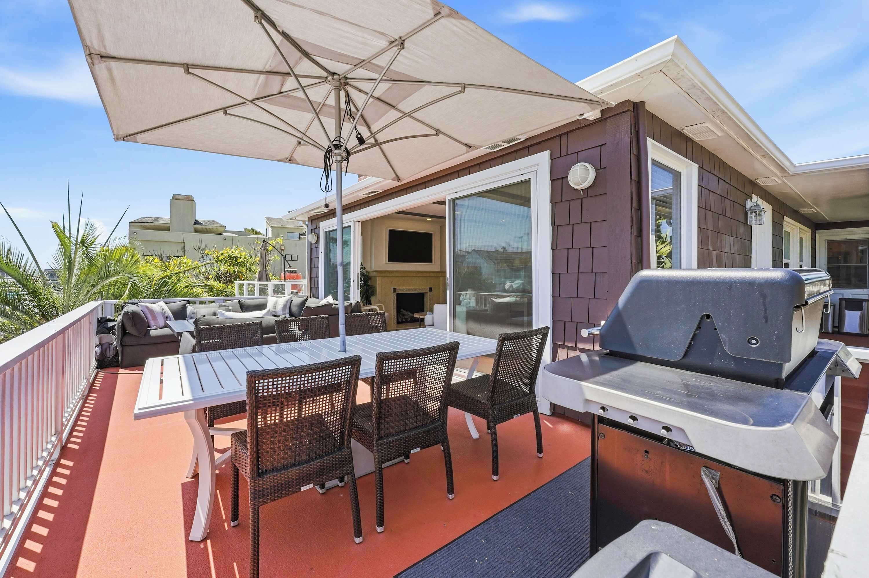 Eine Terrasse im Freien mit Tisch, Stühlen, einem Grill und einem überdachten Bereich mit Sonnenschirm.
