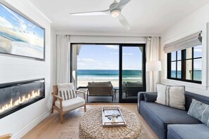 A modern living room with a fireplace, a ceiling fan, a sofa, a chair, and a view of the ocean. - N Oceanfront Masterpiece with Rooftop & Hot Tub + Sauna (San Diego)