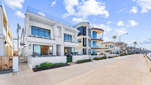 Um edifício residencial moderno com estrutura de dois andares, janelas amplas e área externa com mesas e cadeiras.