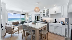 Uma cozinha moderna com armários brancos, uma ilha grande e vista para o oceano.