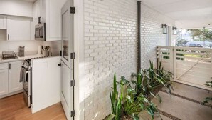 A modern kitchen with white cabinetry, a brick wall, and a small garden area with plants. - Neptune Charm  Coastal (Encinitas)