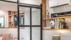 A room with a sliding glass door, a round table, a sofa, a lamp, and shelves with books and decorative items. - Neptune Charm  Coastal (Encinitas)