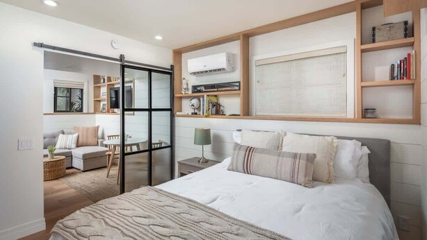 A bedroom with a large bed, a sliding door leading to a living area, and built-in shelving with books and decorative items. - Neptune Charm  Coastal (Encinitas)