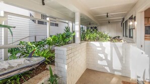 A covered outdoor area with a brick wall, potted plants, and a hammock. - Neptune Charm  Coastal (Encinitas)