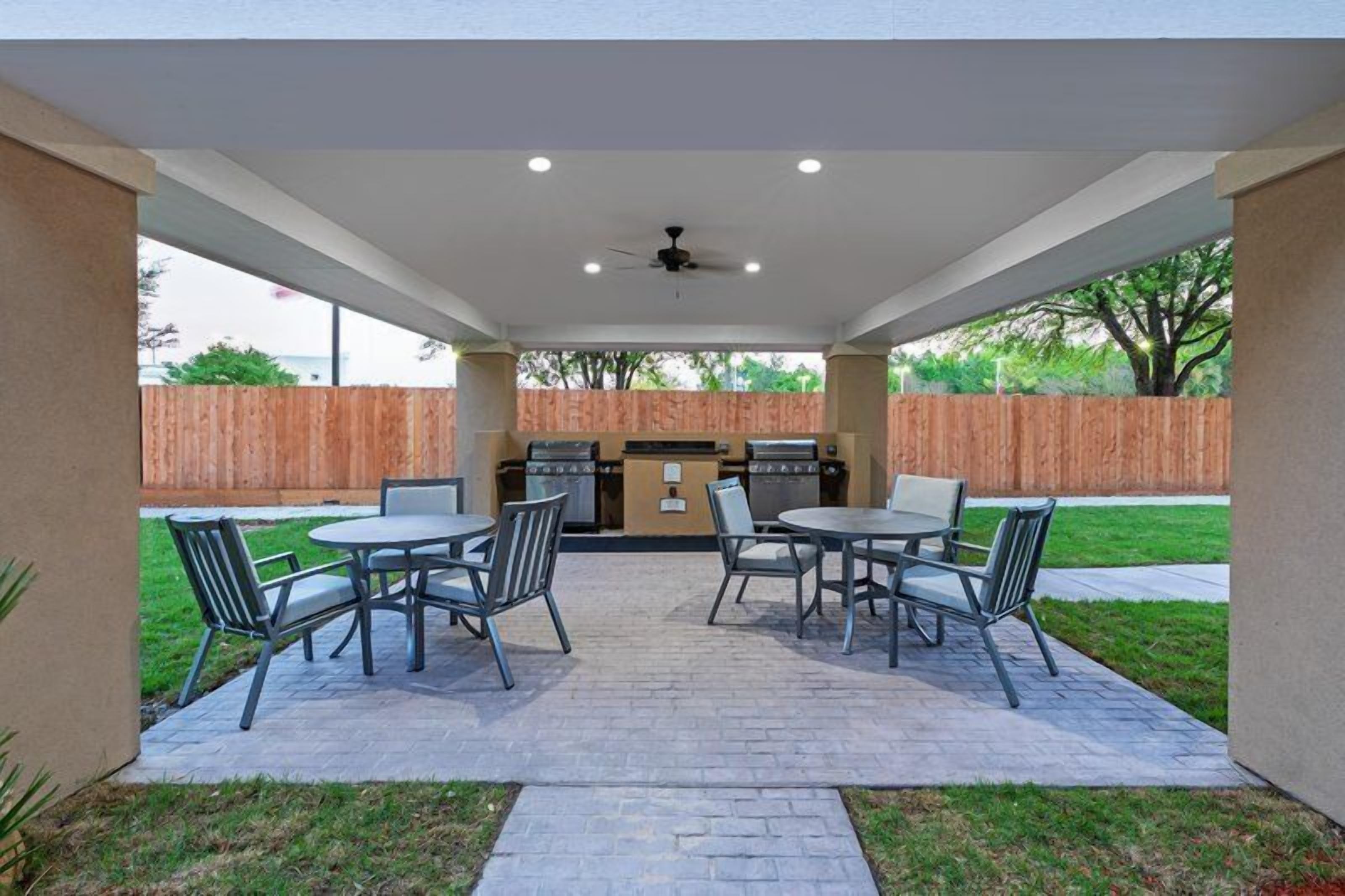 An outdoor patio with a grill, four tables, and chairs.