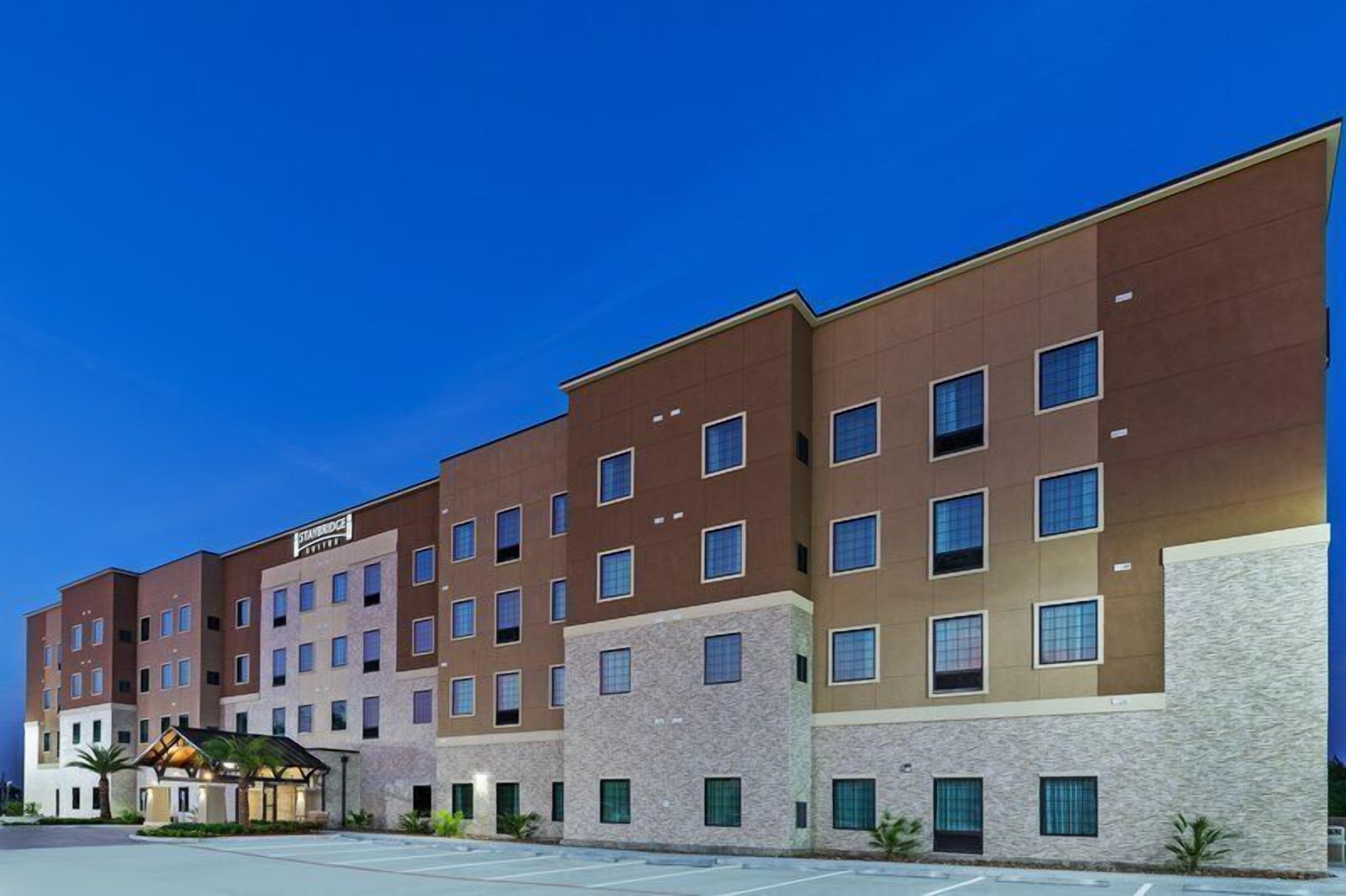 A multi-story hotel with a modern design, featuring a mix of brick and stone facades, multiple windows per floor, and a parking lot in front.