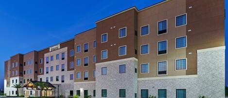 A multi-story hotel with a modern design, featuring a mix of brick and stone facades, multiple windows per floor, and a parking lot in front.