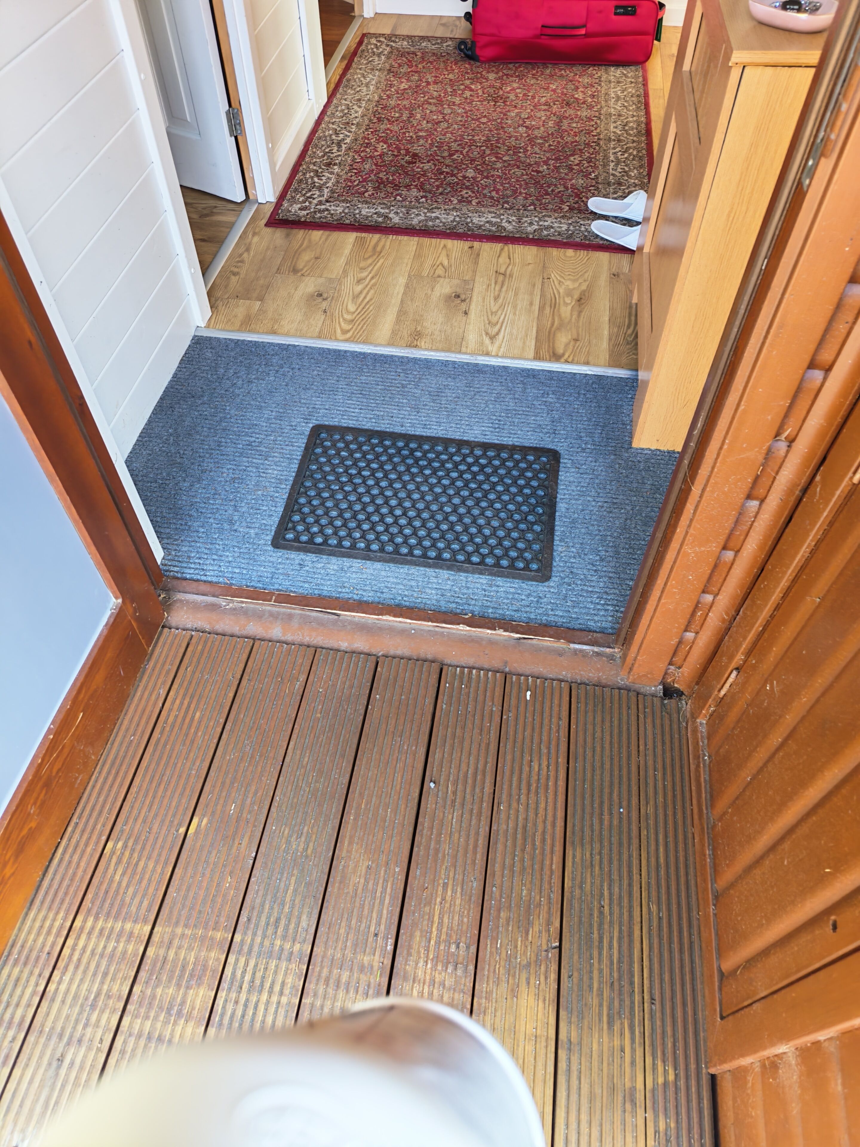 Piso de madeira que leva a um quarto com um tapete azul, uma bolsa vermelha e uma cadeira branca.