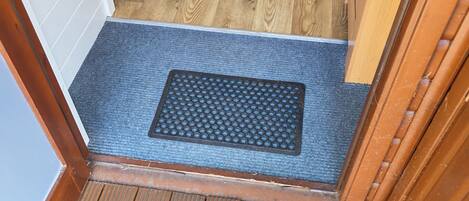 Piso de madeira que leva a um quarto com um tapete azul, uma bolsa vermelha e uma cadeira branca.