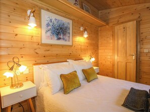 Quarto de madeira com cama, luminárias de cabeceira, mesa de cabeceira, um quadro na parede e uma porta.